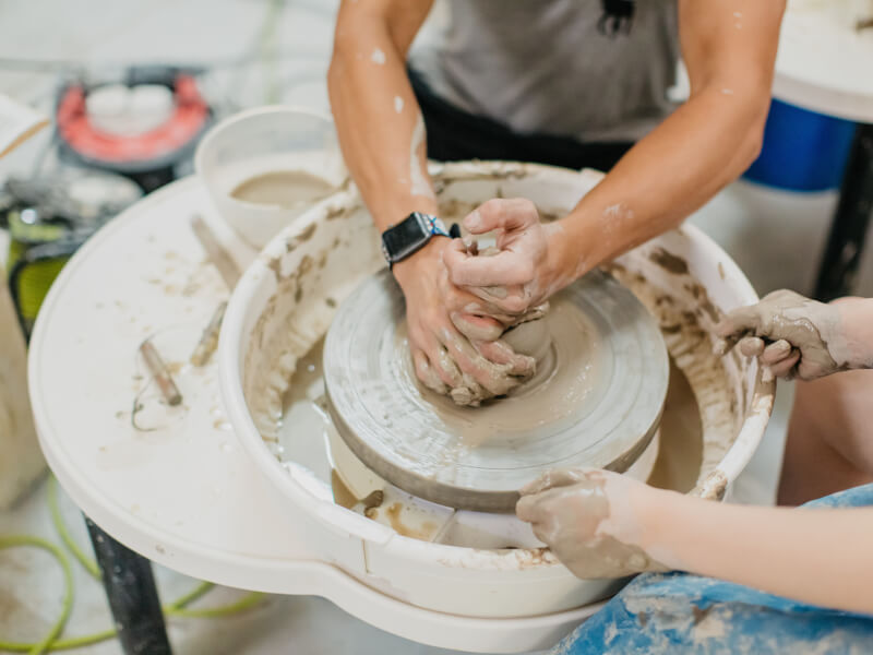 A closeup of two people using a potter's wheel together